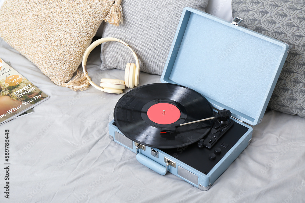 Record player with vinyl disk and headphones on bed in room