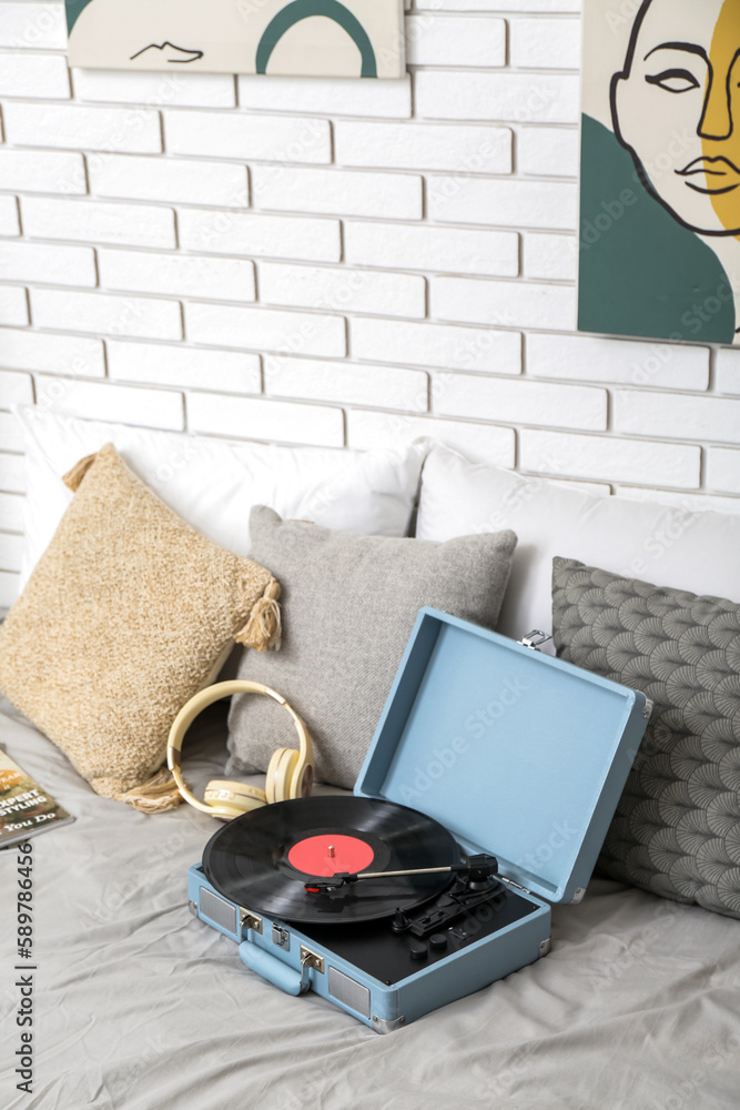 Record player with vinyl disk and headphones on bed in room