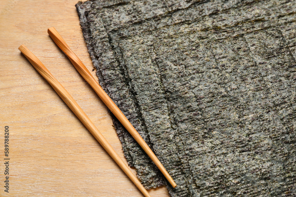 Wooden board with nori sheets and chopsticks, closeup