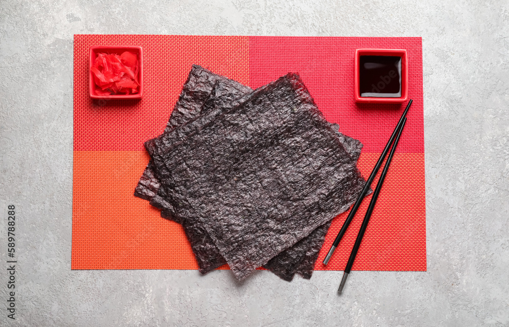 mat with nori sheets, ginger, soy sauce and chopsticks on light background