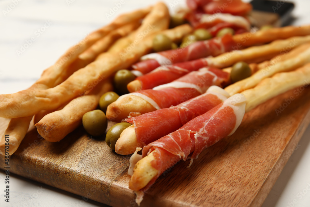 Wooden board of tasty Italian Grissini with bacon on table, closeup