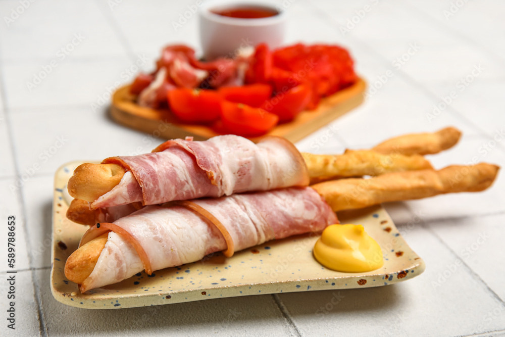 Plate of tasty Italian Grissini with bacon on white tile background, closeup