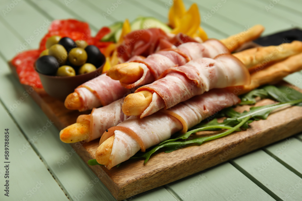 Board of tasty Italian Grissini with bacon on green wooden background, closeup