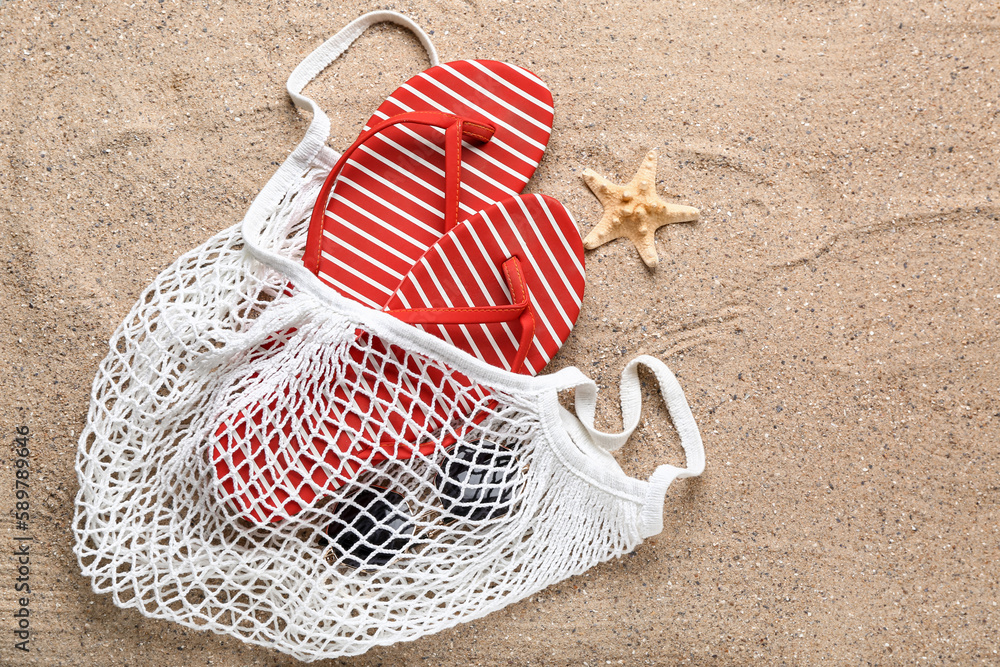 String bag with flip-flops, sunglasses and starfish on sand