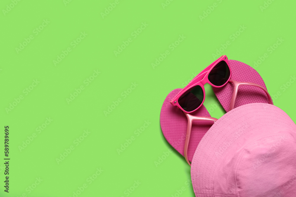 Flip-flops with sunglasses and bucket hat on green background