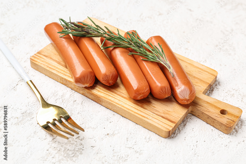 Wooden board with tasty sausages on light background