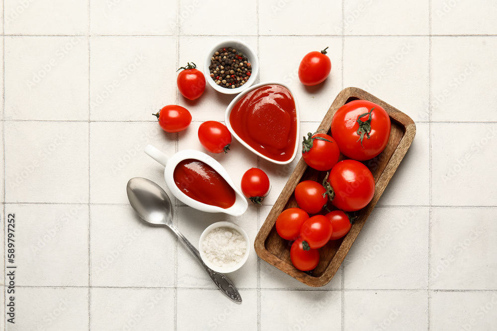 Gravy boat and bowl of tasty ketchup with fresh tomatoes on white tile background