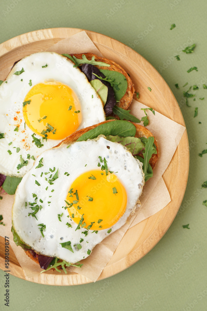 Delicious sandwiches with fried eggs on green background