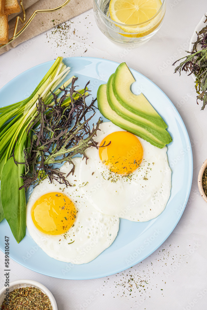 Plate with tasty fried eggs and greens on light table