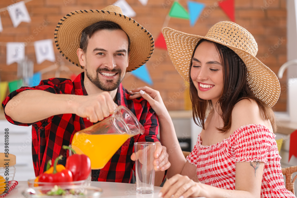 Young couple with juice celebrating Festa Junina (June Festival) in kitchen