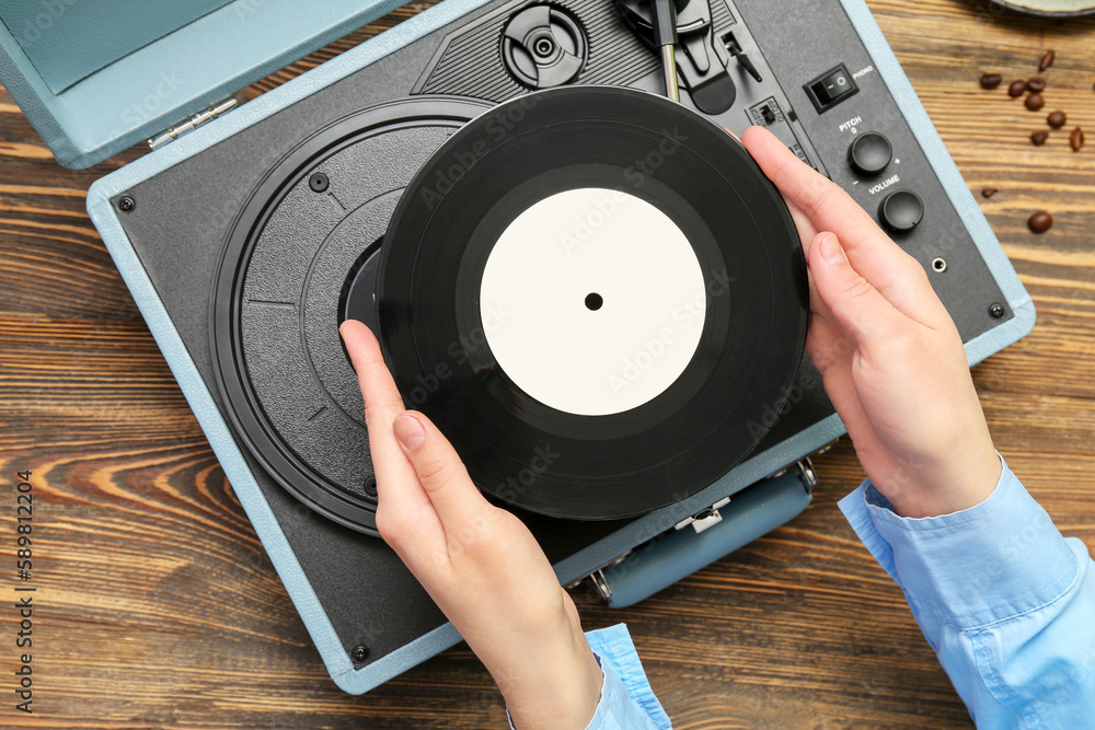 Woman with vinyl disk and record player on wooden background, closeup