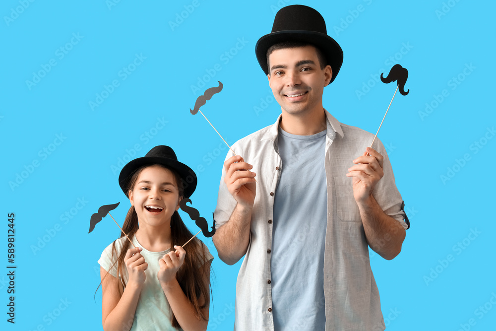 Portrait of father and his little daughter with paper mustache on light blue background