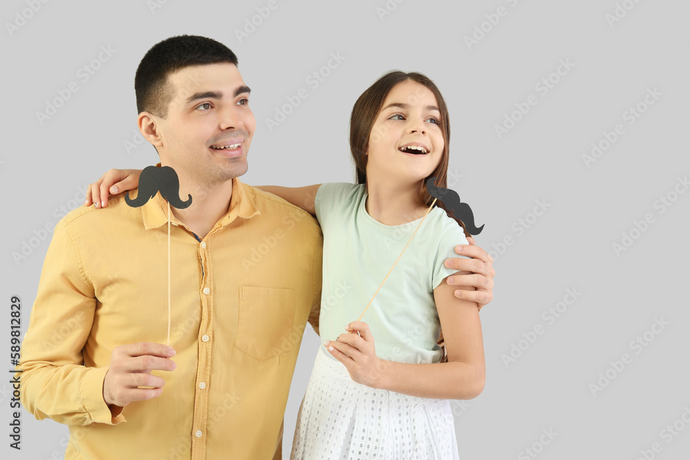 Portrait of father and his little daughter with paper mustache on light background