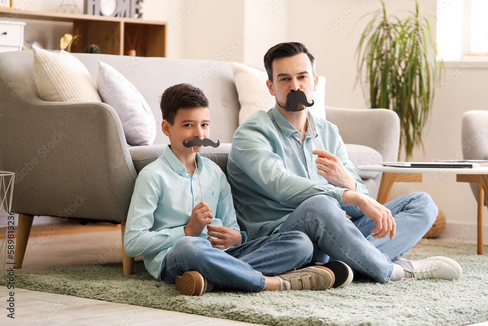 Portrait of father and his little son with paper mustache at home