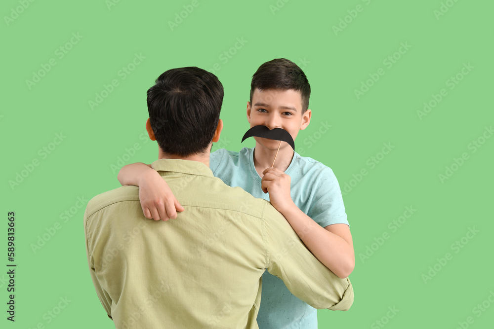 Father and his little son with paper mustache on green background