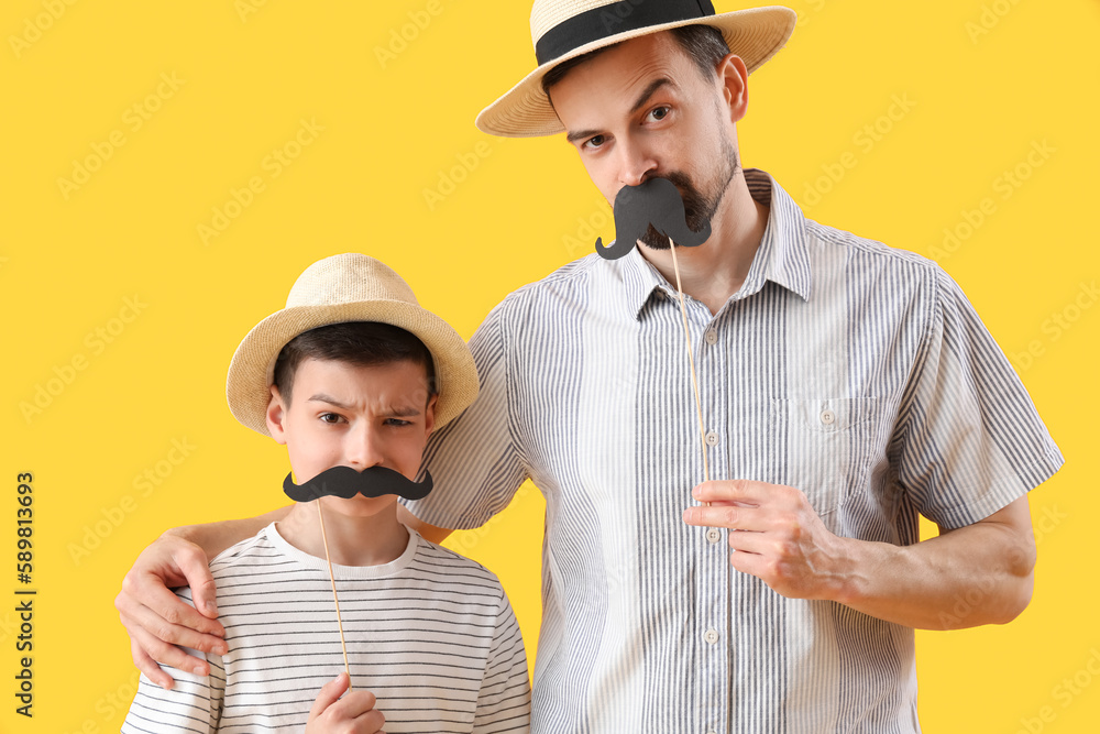 Portrait of funny father and his little son with paper mustache on yellow background