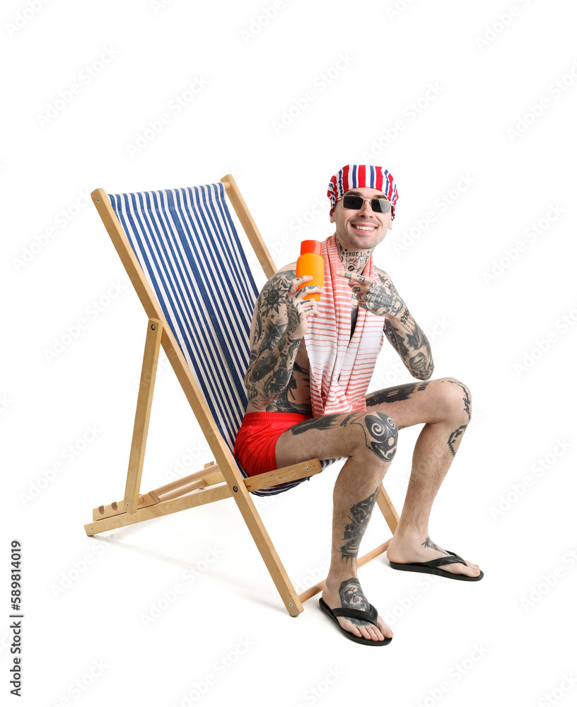 Tattooed man with sunscreen cream sitting on deck chair against white background