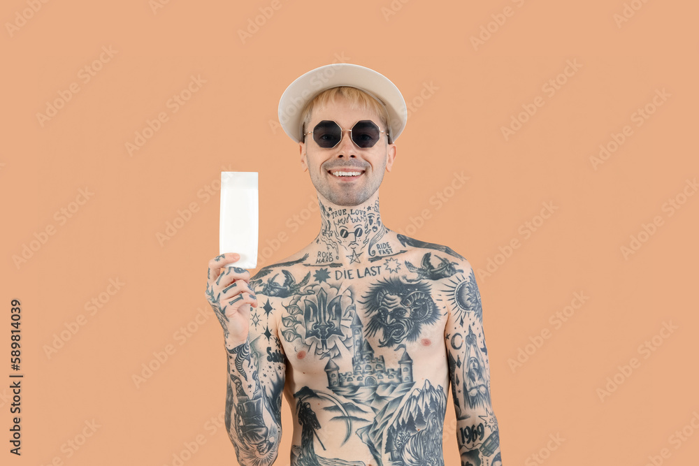 Tattooed man with sunscreen cream on beige background