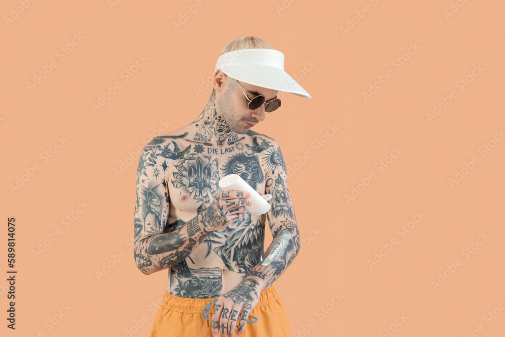 Tattooed man applying sunscreen cream on beige background