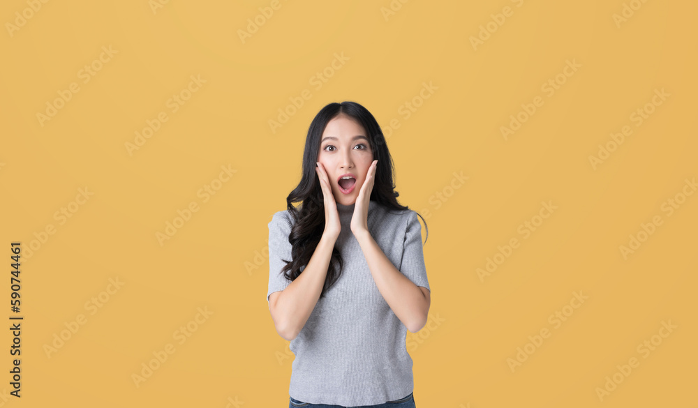 Young Asian doing a shocked surprise gesture with her hands on her face isolated yellow color backgr