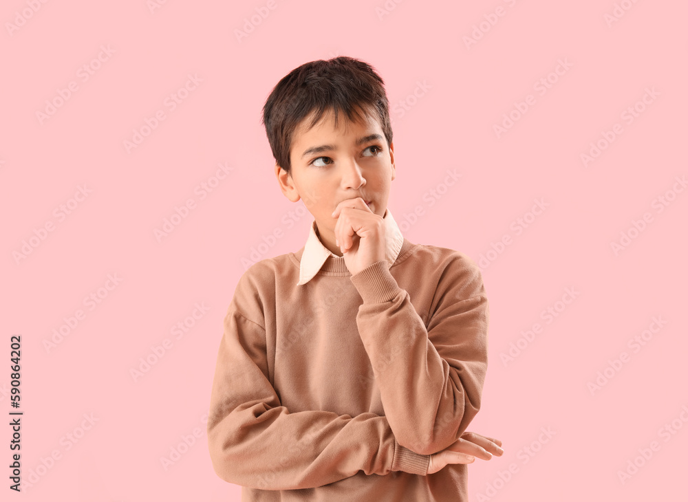 Little boy biting nails on pink background