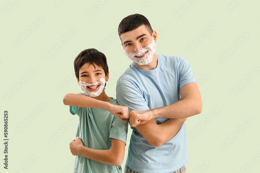 Man and his little son with shaving foam on faces bumping fists against light color background