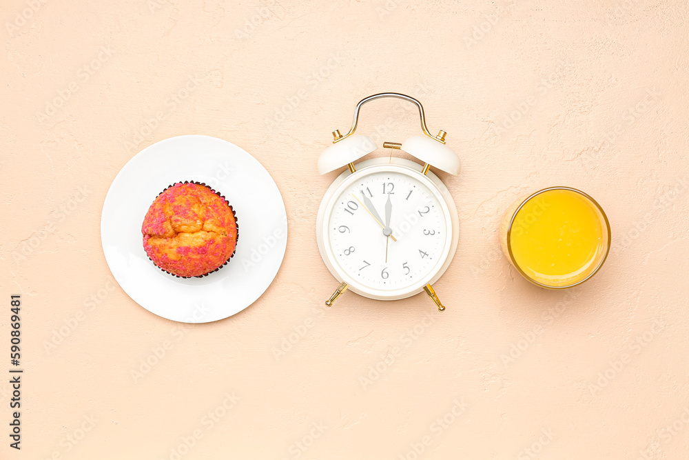 Tasty muffin,alarm clock and glass of juice on color background