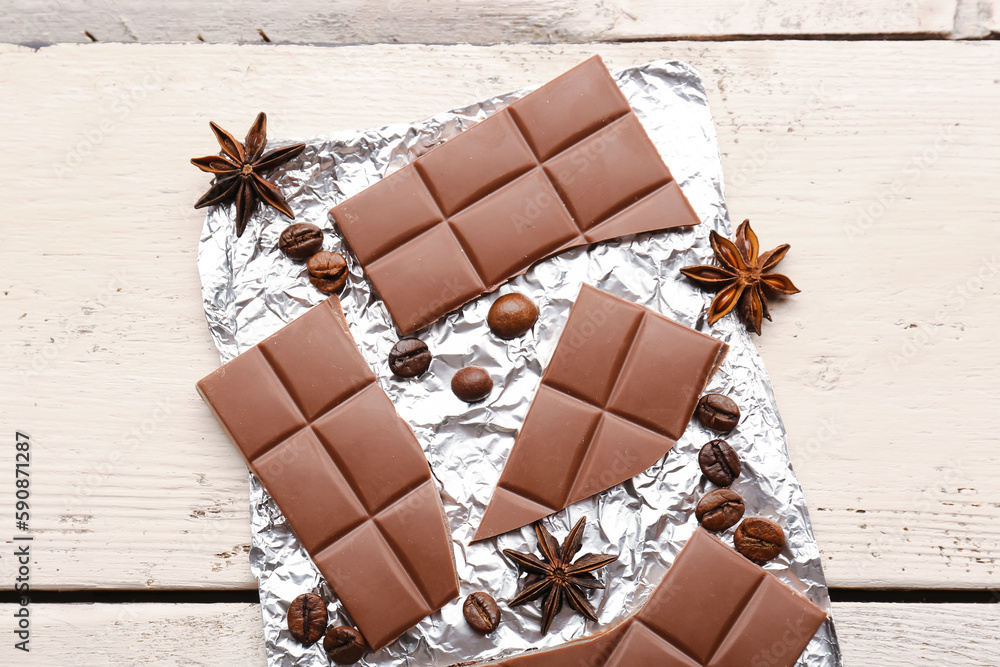 Foil with tasty chocolate, coffee beans and anise stars on light wooden background