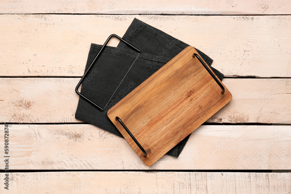 Cutting board with cheese slicer and napkin on light wooden background