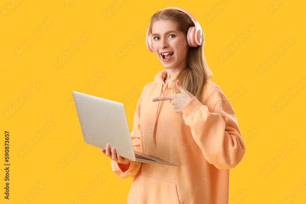 Female programmer in headphones pointing at laptop on yellow background