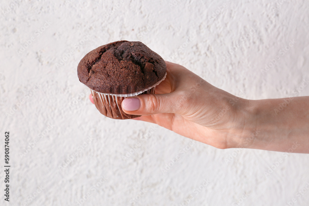 Woman holding tasty chocolate cupcake on light background