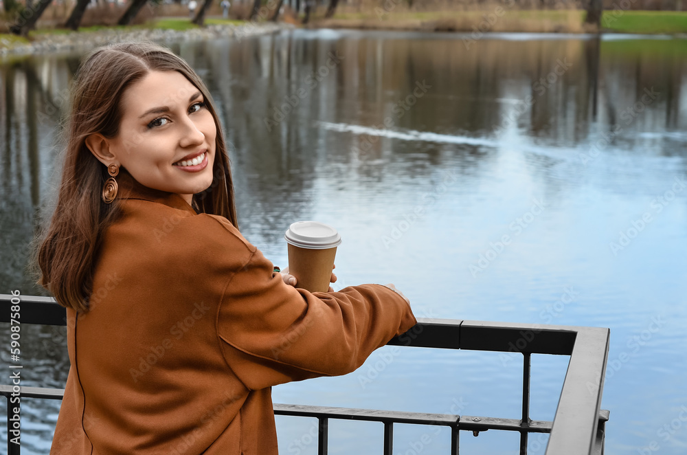 Stylish young woman with cup of coffee on embankment