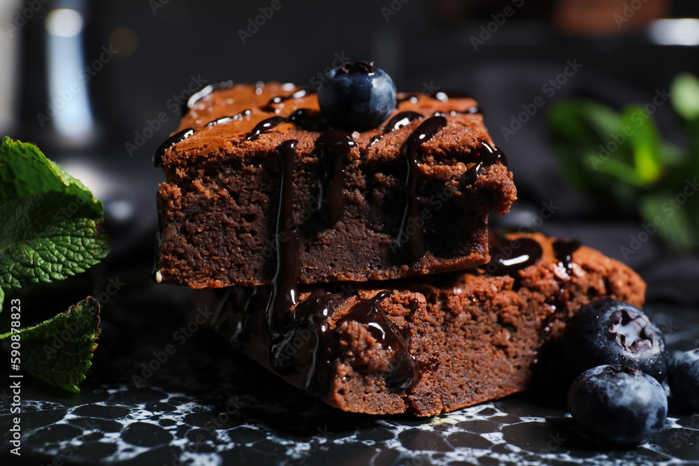 Board with pieces of tasty chocolate brownie on black background, closeup