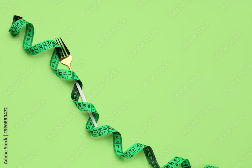 New measuring tape and fork on green background