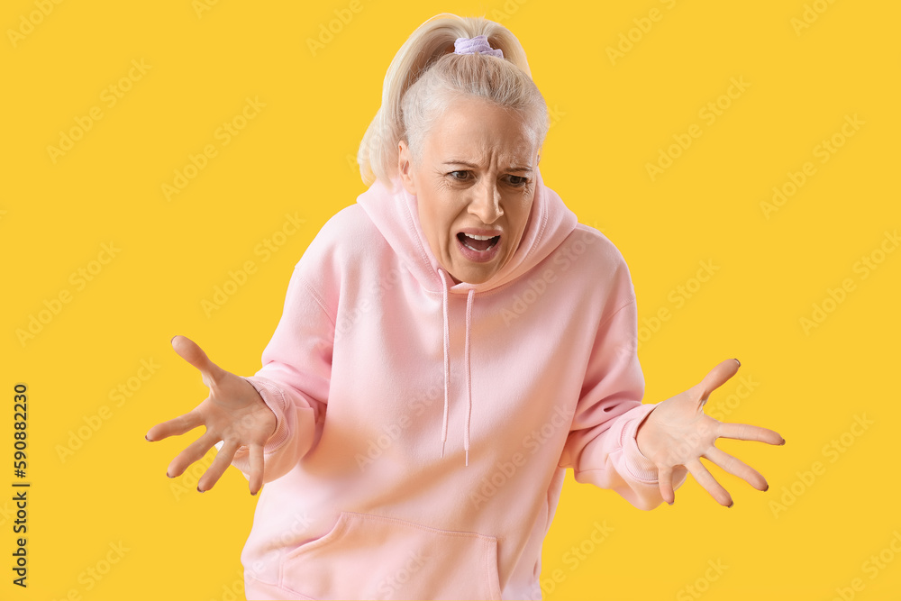 Angry mature woman on yellow background