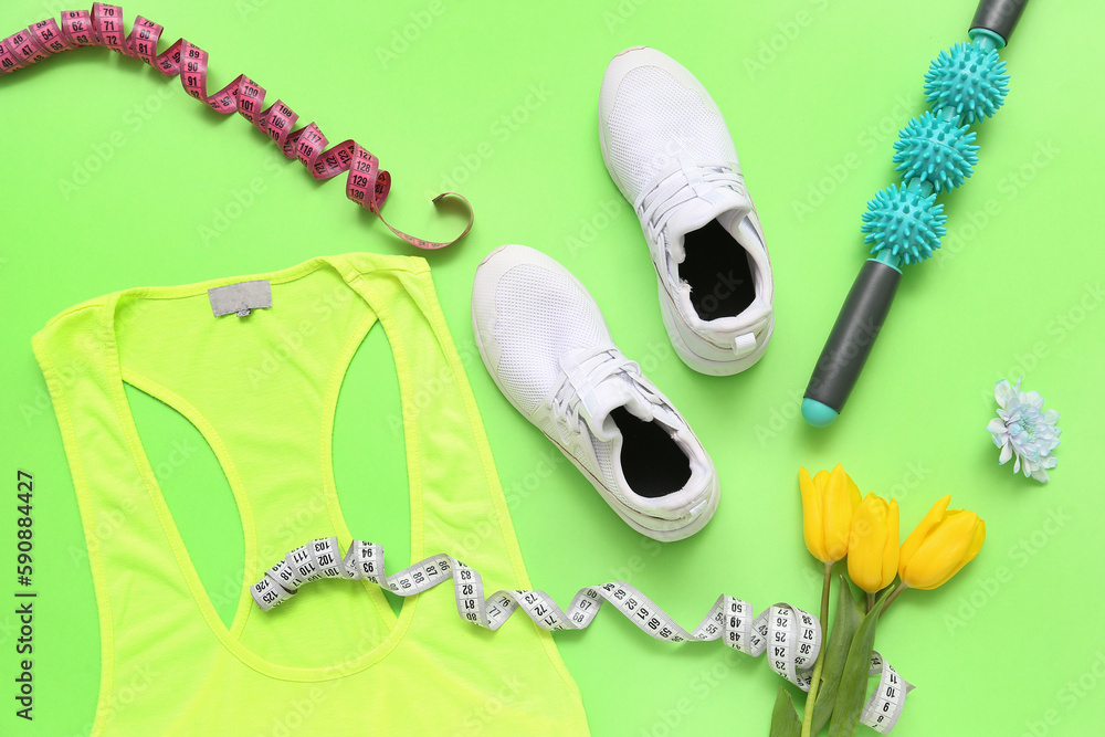 Sneakers with spring flowers, massage roller, measuring tapes and sportswear on green background