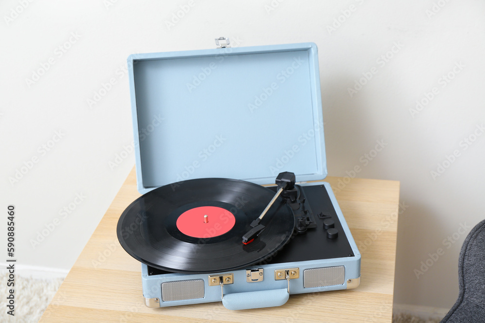 Record player with vinyl disk on table near light wall in room