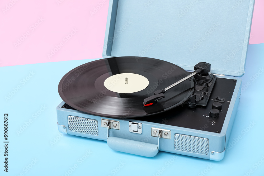 Record player with vinyl disk on table near pink wall