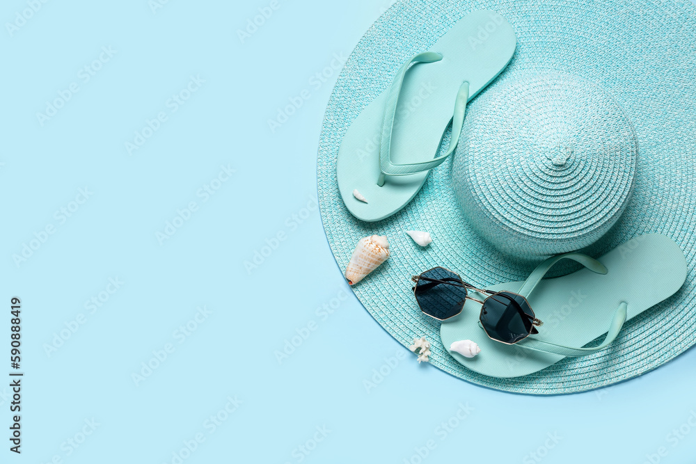 Flip-flops with sunglasses, seashells and hat on blue background