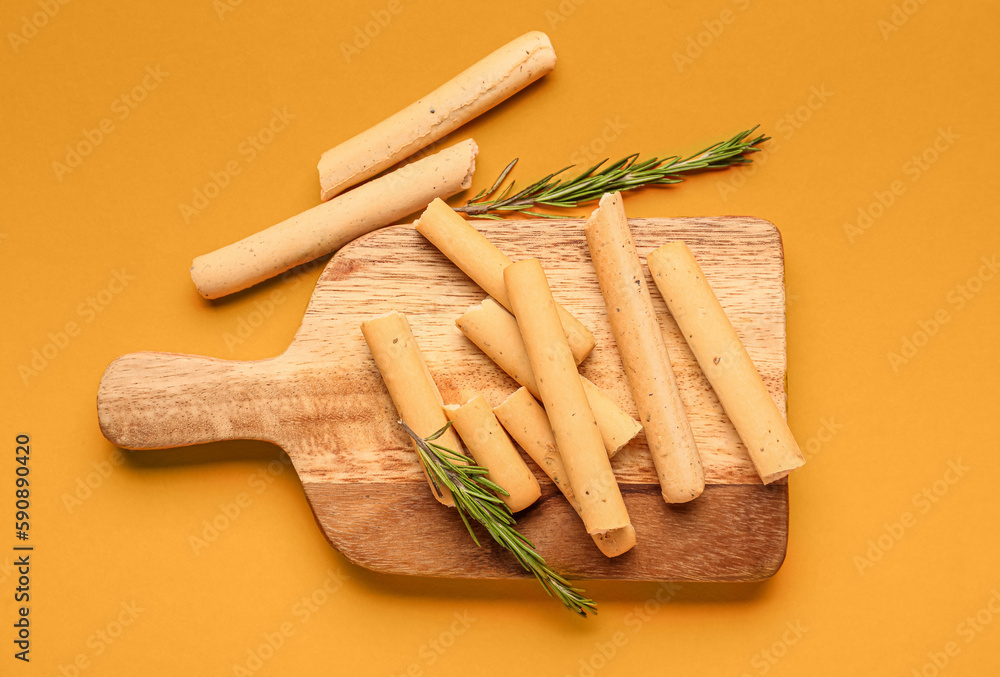 Wooden board with tasty Italian Grissini on orange background