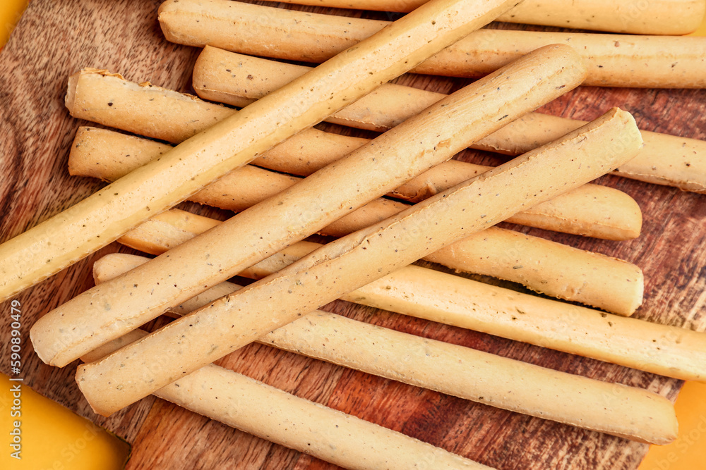 Wooden board with tasty Italian Grissini on orange background, closeup