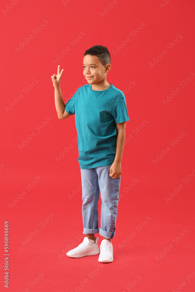 Little African-American boy showing peace gesture on red background