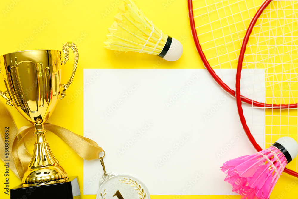 Blank card with gold cup and badminton equipment on yellow background, closeup