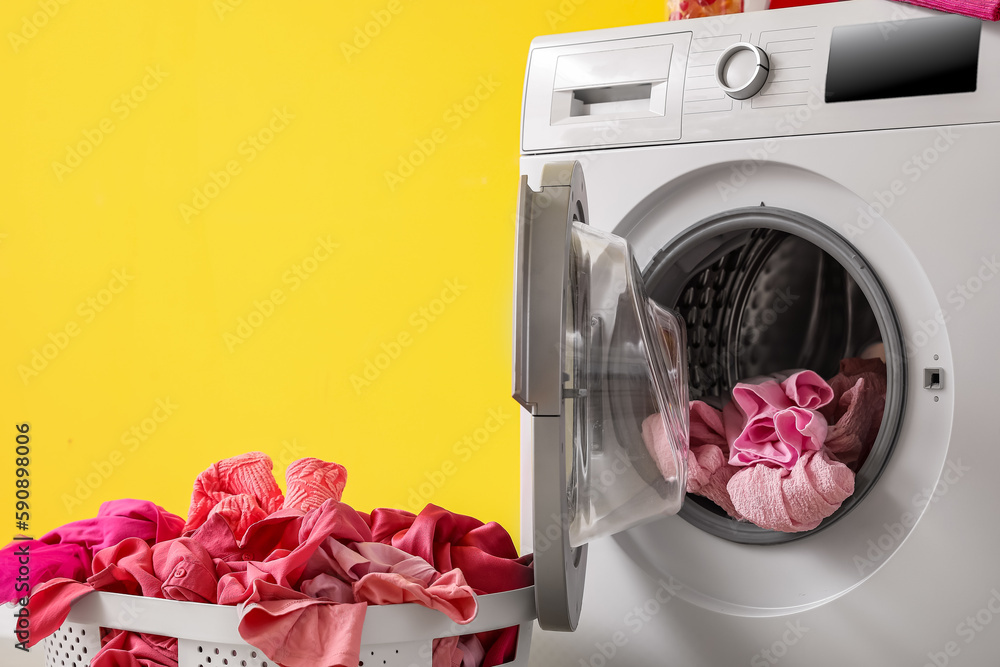 laundry basket with dirty clothes and washing machine near yellow wall, closeup