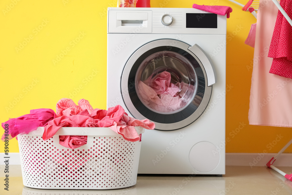 Basket with dirty clothes and washing machine in laundry room