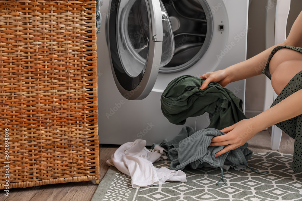 Woman putting dirty clothes into washing machine in laundry room, closeup