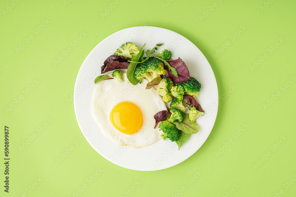 Plate with tasty fried egg, broccoli and spinach on green background