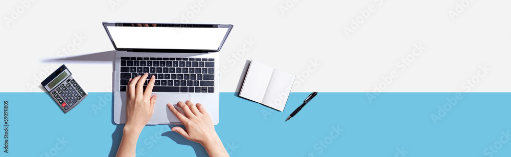 Person using a laptop computer with a notebook and a calculator