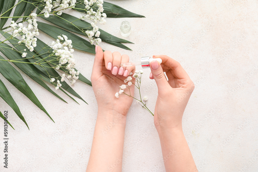 Female hands with bottle of cuticle oil, gypsophila flowers and palm leaf on light background