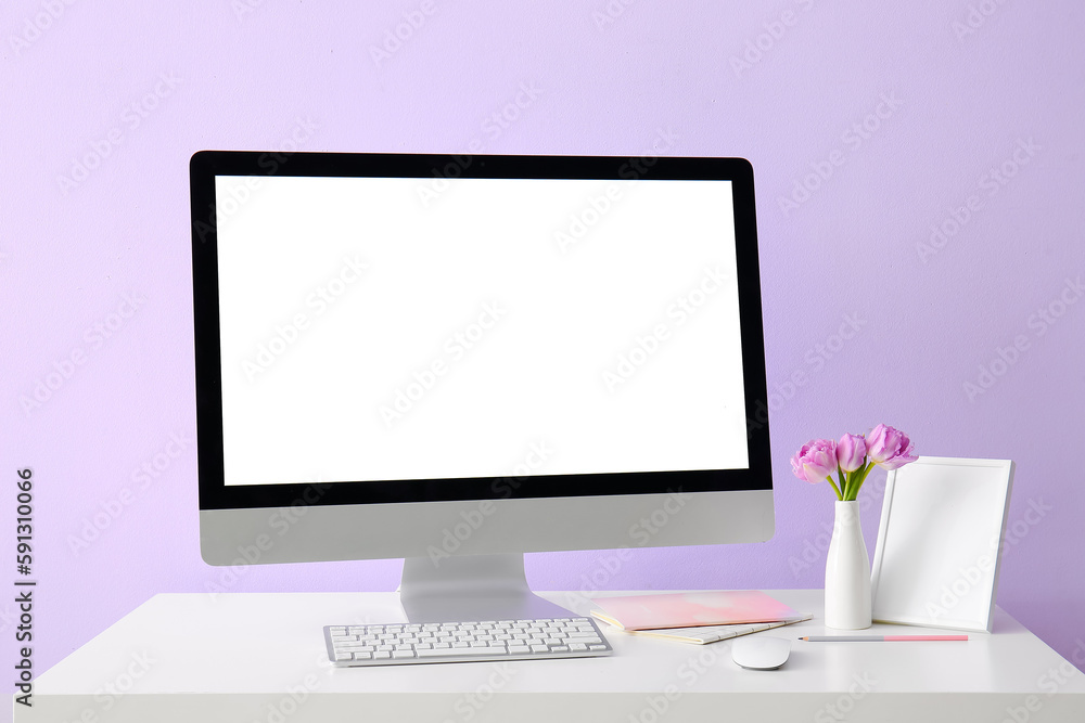 Workplace with computer, tulips in vase and frame near lilac wall